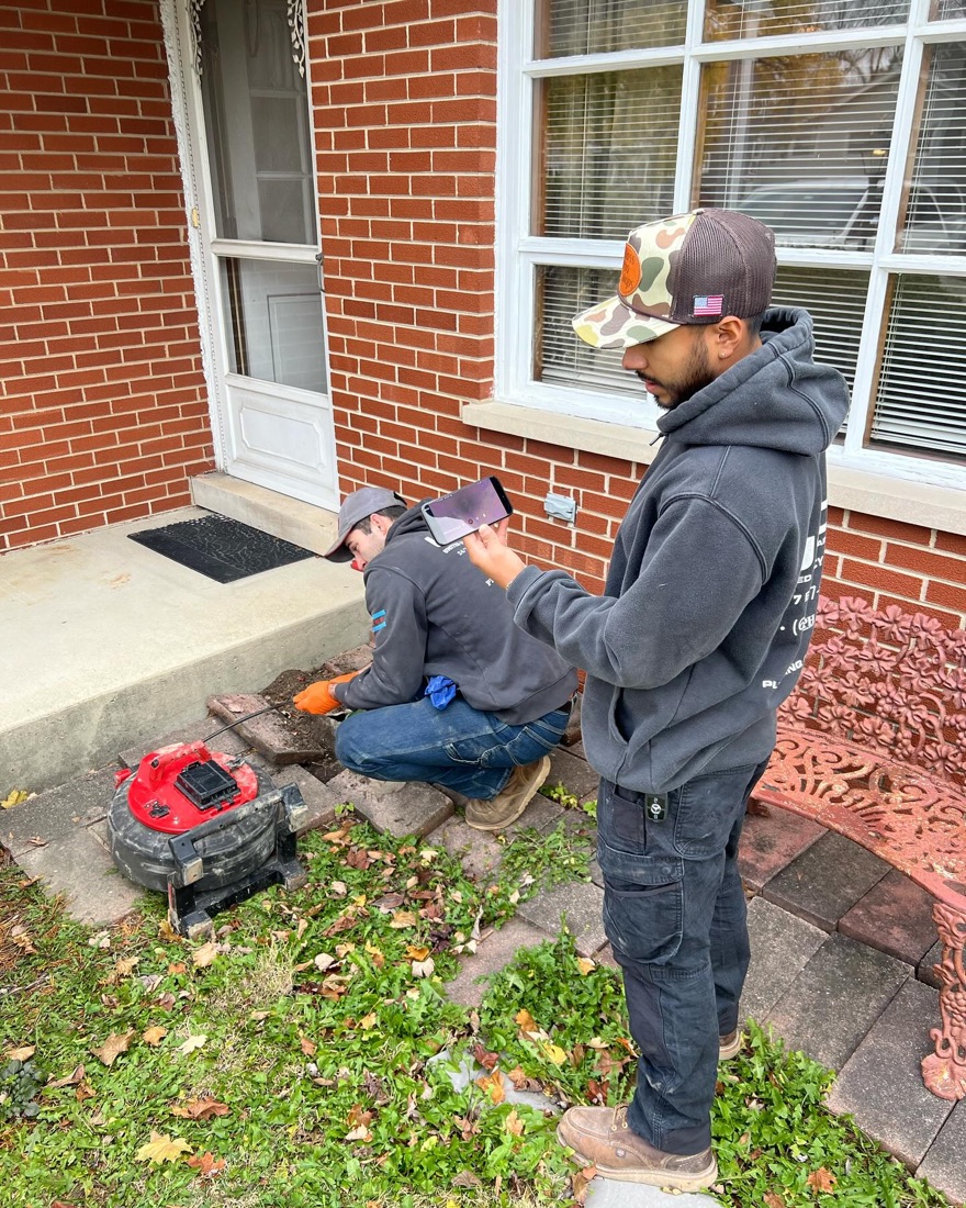 Two USDS techs running a camera reel on a sewer lateral, reading the monitor