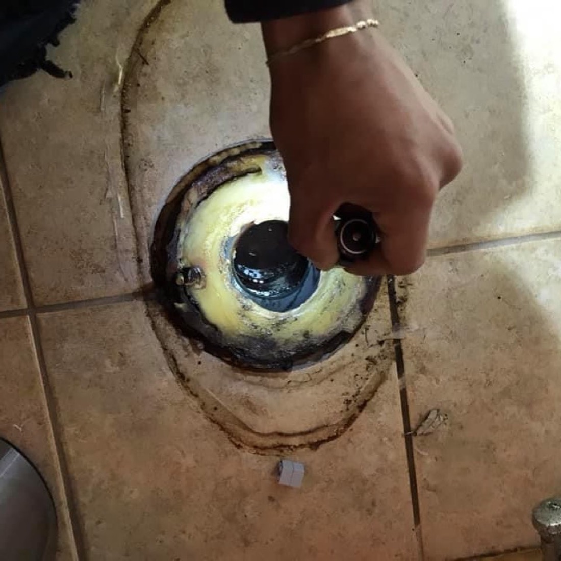 Technician reaching into an opened floor-level drain access in a tiled bathroom
